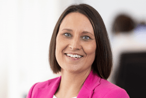 Woman with short brown hair and a pink shirt smiles at the camera