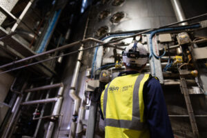 Factory worker in hard hat stands underneath boiler