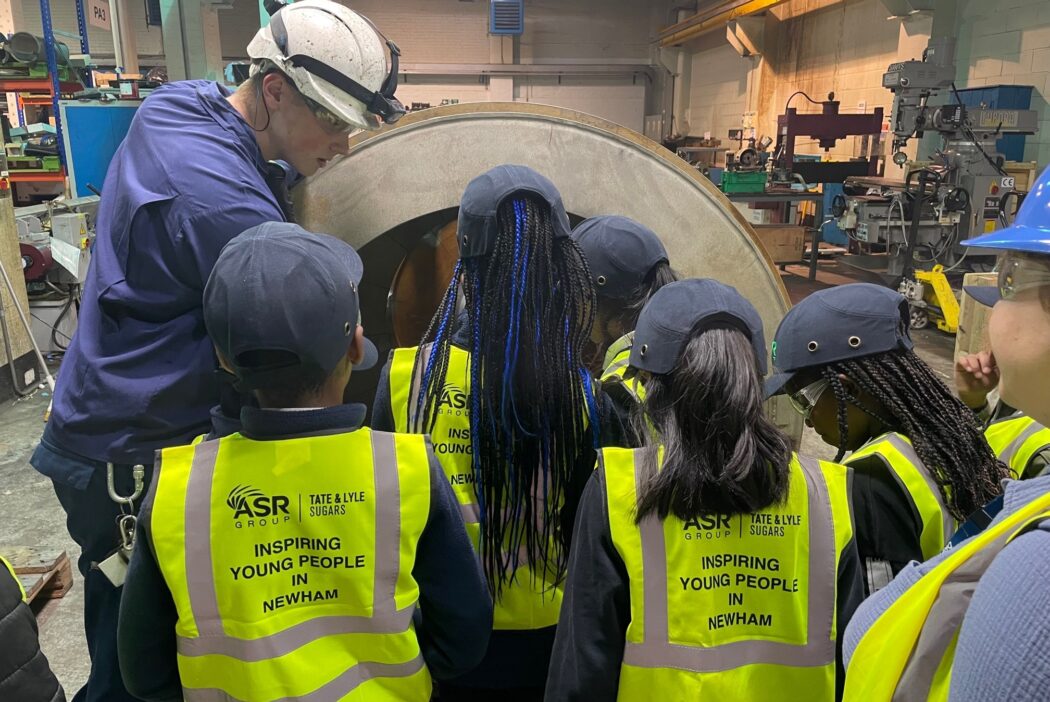 Children wearing hi vis vests look at a piece of equipment in an engineering workshop