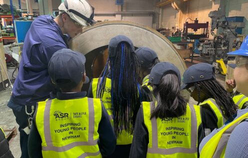 Children wearing hi vis vests look at a piece of equipment in an engineering workshop