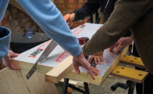 People working at a work bench using a saw and ruler