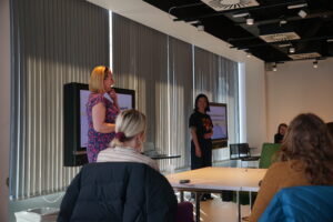 A meeting room containing a screen and a presenter talking to the audience