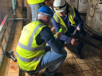 Two workers in hi visibility vests crouch down and look at a pipe