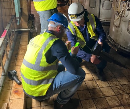 Two workers in hi visibility vests crouch down and look at a pipe