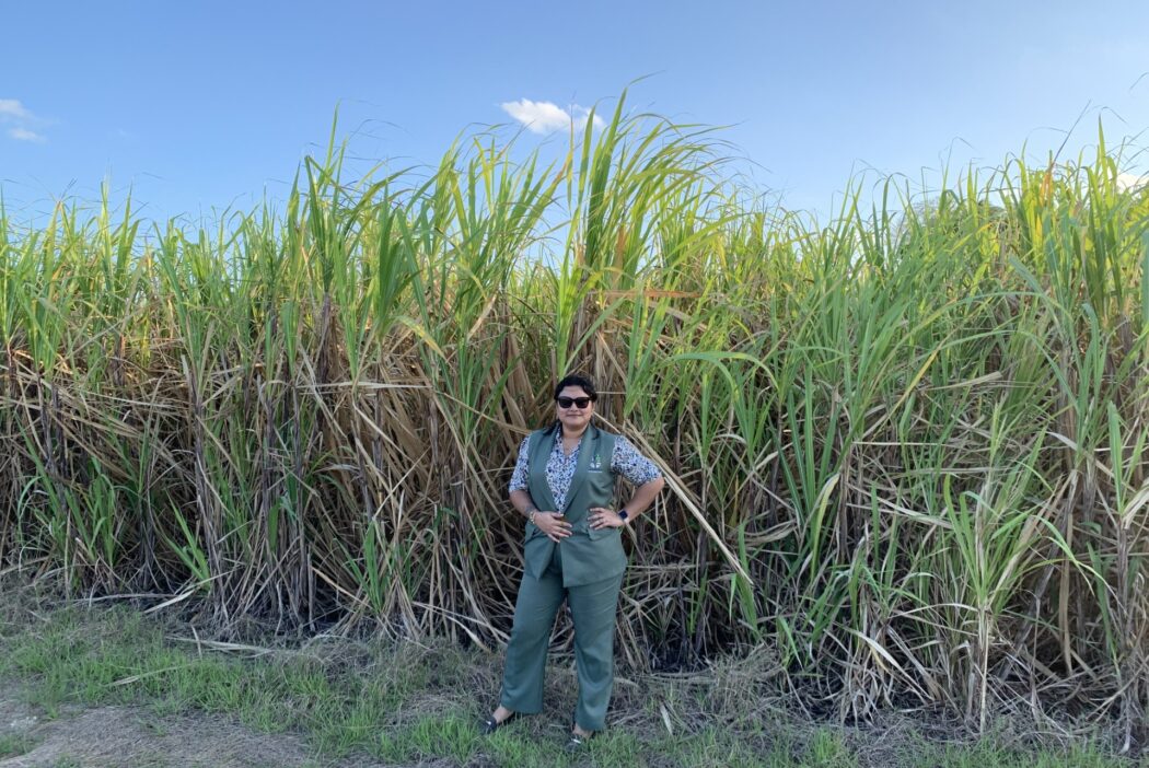 A women in sunglasses stands in front of sugar cane