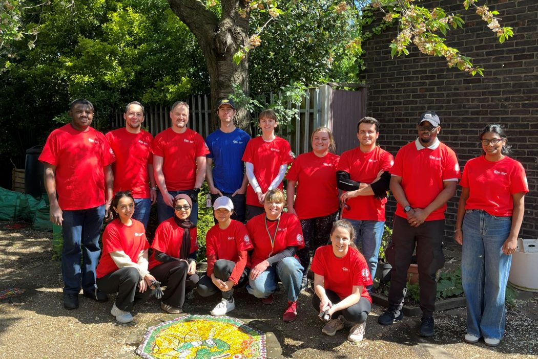 Tate & Lyle Sugars Volunteers wearing red Earth Day shirts stand together in front of the community garden