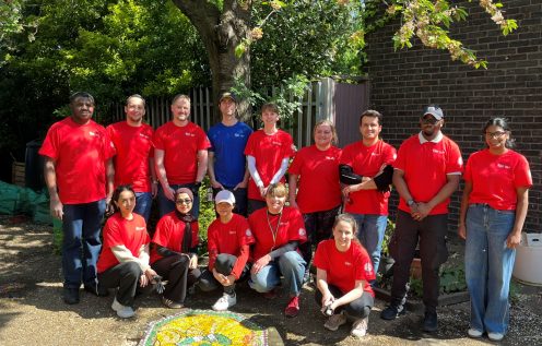 Tate & Lyle Sugars Volunteers wearing red Earth Day shirts stand together in front of the community garden