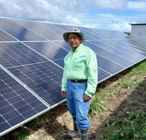 A man stands next to large solar panels on a field