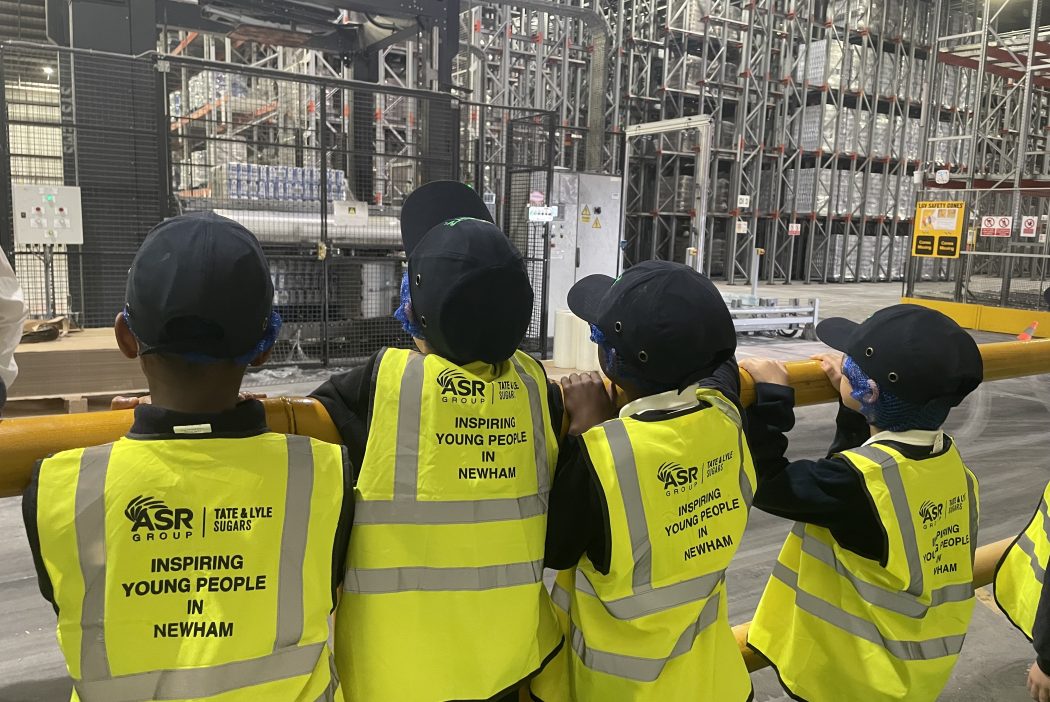 Students in hi-vis that reads Inspiring Young People in Newham stand looking into a warehouse