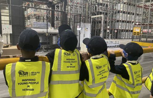 Students in hi-vis that reads Inspiring Young People in Newham stand looking into a warehouse