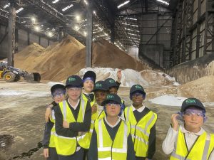 Students in hi-vis jackets stand in front of piles of raw sugar in a warehouse
