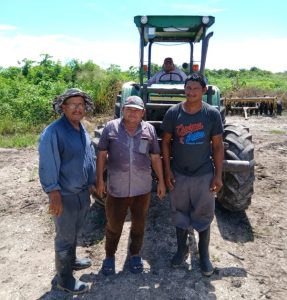 Three sugarcane farmers in front of a tractor in a field of sugarcane