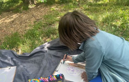 Boy colouring in on a mat in the woods