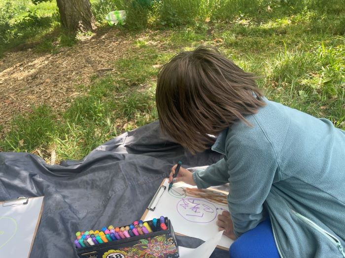 Boy colouring in on a mat in the woods